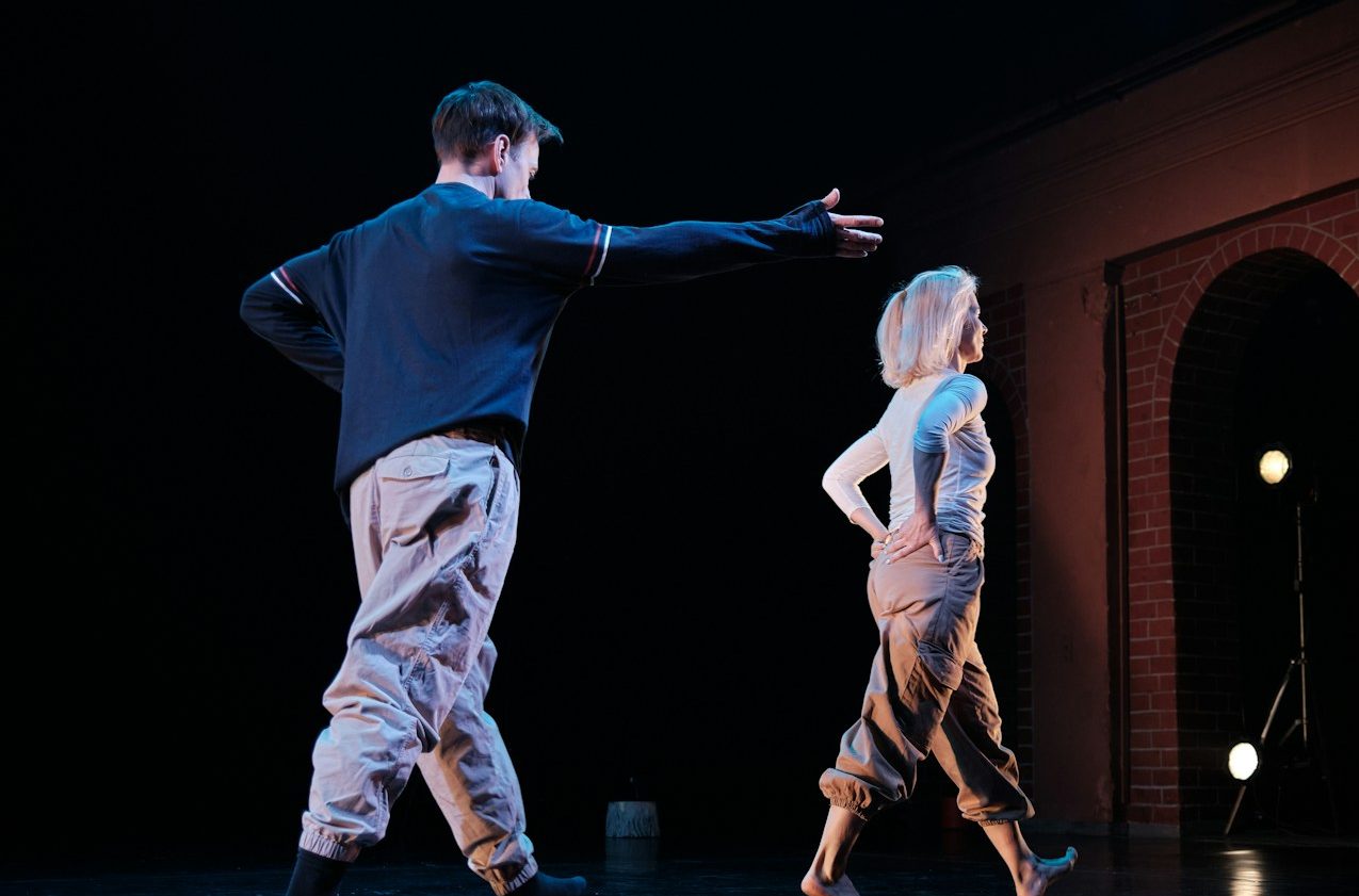 A women walking away from a man dressed in casual clothes on a dark stage.