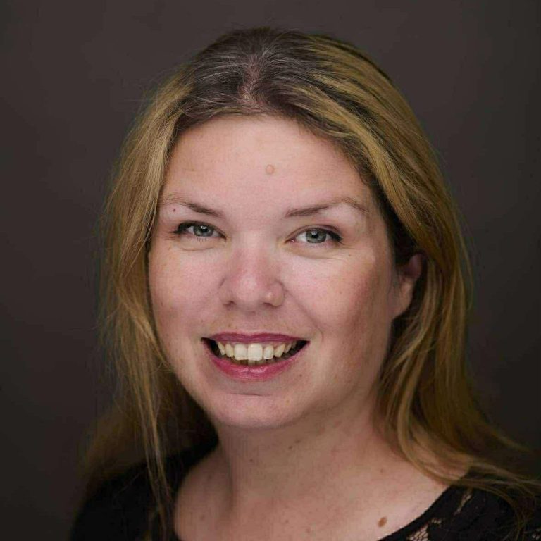 A woman with short black hair smiles happily at the camera.